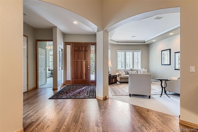 entrance foyer featuring arched walkways, wood finished floors, baseboards, a raised ceiling, and recessed lighting