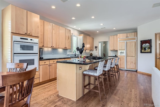 kitchen featuring paneled fridge, light brown cabinetry, white double oven, light wood-style floors, and recessed lighting