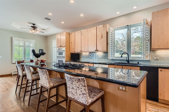 kitchen featuring a sink, a baseboard heating unit, white appliances, light brown cabinets, and light wood finished floors