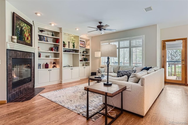 living room featuring a tiled fireplace, healthy amount of natural light, wood finished floors, and a ceiling fan