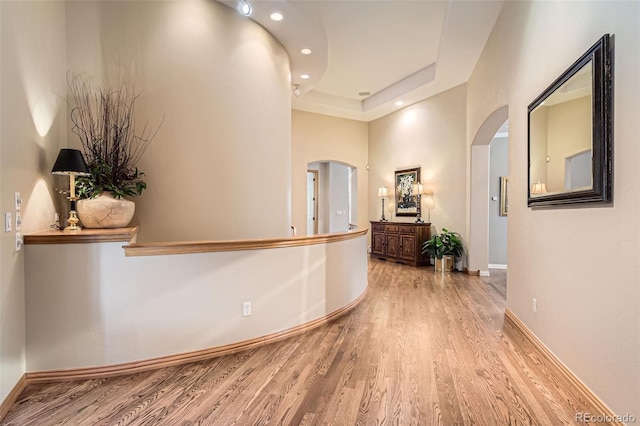 hallway featuring arched walkways, light wood finished floors, baseboards, and recessed lighting