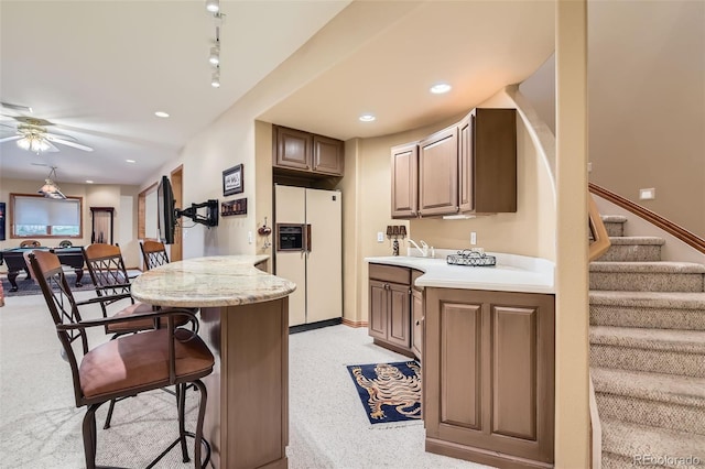 kitchen with white refrigerator with ice dispenser, a breakfast bar, a peninsula, light countertops, and ceiling fan