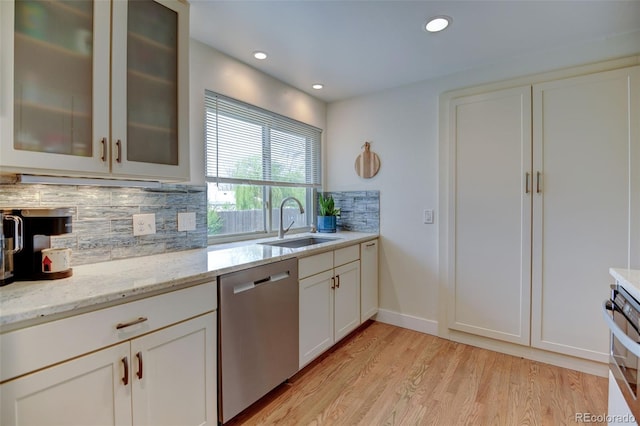 kitchen with tasteful backsplash, stainless steel dishwasher, light stone countertops, light wood-type flooring, and a sink