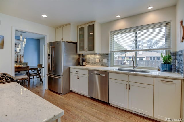 kitchen featuring backsplash, appliances with stainless steel finishes, light wood-type flooring, a sink, and white cabinets