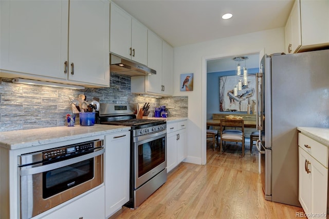 kitchen with light wood-type flooring, under cabinet range hood, white cabinets, tasteful backsplash, and stainless steel appliances