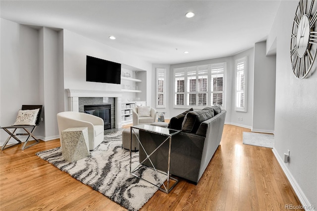 living area featuring a fireplace with flush hearth, built in features, baseboards, and wood finished floors