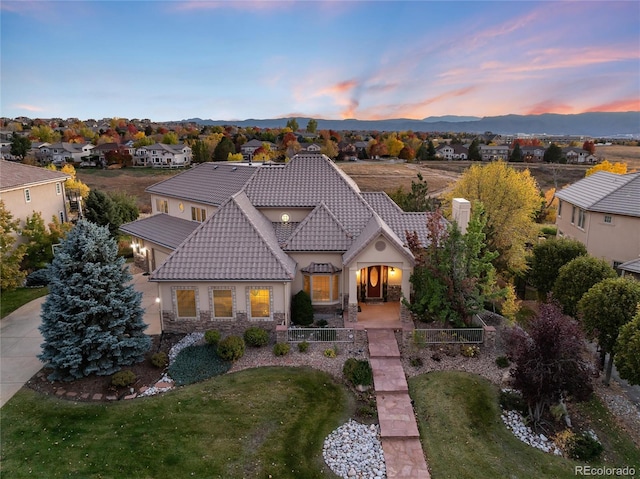 view of front of house featuring stone siding, a tile roof, a fenced front yard, stucco siding, and a front yard