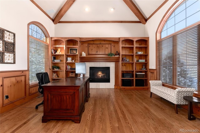 office space with lofted ceiling with beams, a healthy amount of sunlight, hardwood / wood-style floors, and a tile fireplace