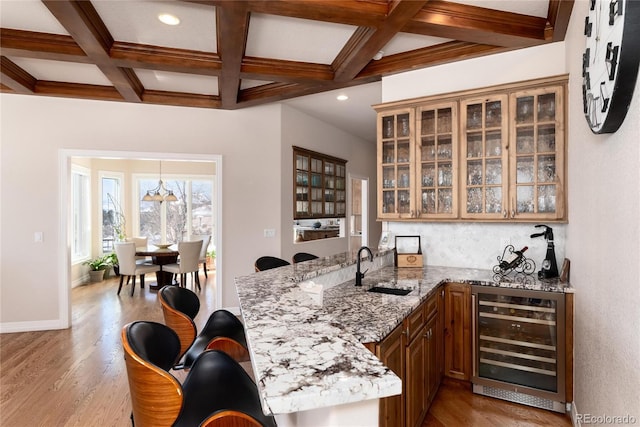 bar with sink, wine cooler, coffered ceiling, light stone counters, and beam ceiling