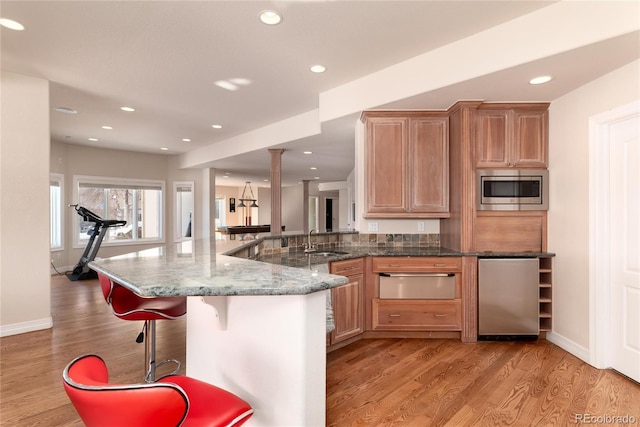 kitchen with sink, a breakfast bar area, refrigerator, stainless steel microwave, and dark stone counters