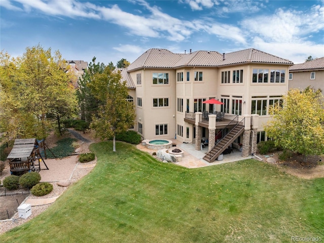 back of property featuring an in ground hot tub, a wooden deck, a patio, and a lawn