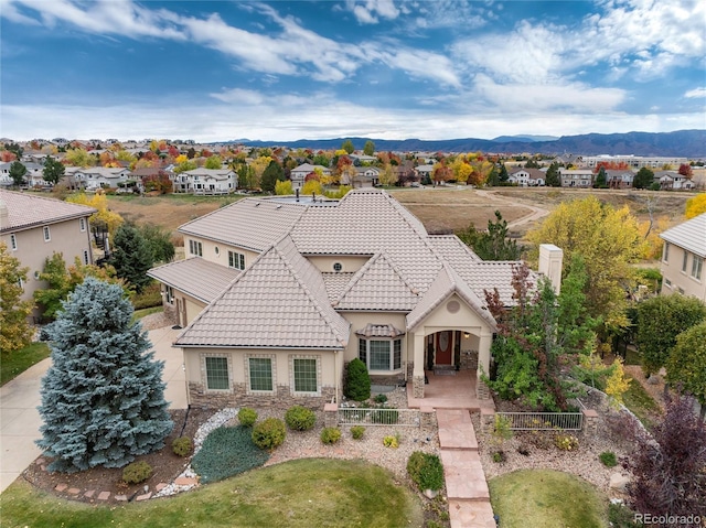 view of front of home featuring stone siding, a tile roof, a fenced front yard, a mountain view, and stucco siding