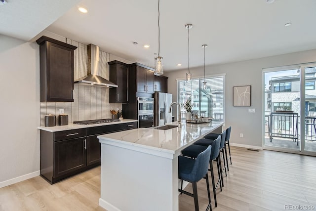 kitchen with hanging light fixtures, tasteful backsplash, wall chimney range hood, a center island with sink, and stainless steel appliances