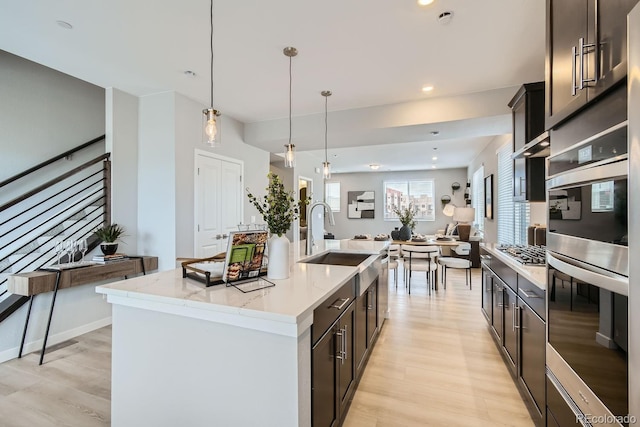 kitchen featuring appliances with stainless steel finishes, light hardwood / wood-style flooring, pendant lighting, light stone counters, and a center island with sink