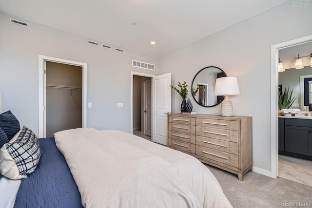 bedroom with a walk in closet, a closet, ensuite bath, and light carpet