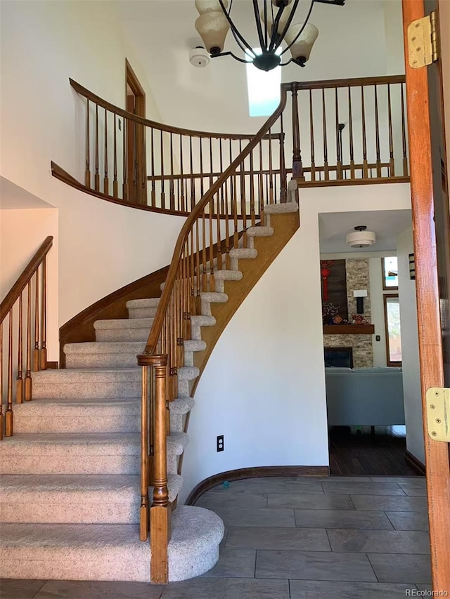 staircase with wood finish floors, baseboards, a stone fireplace, and a towering ceiling