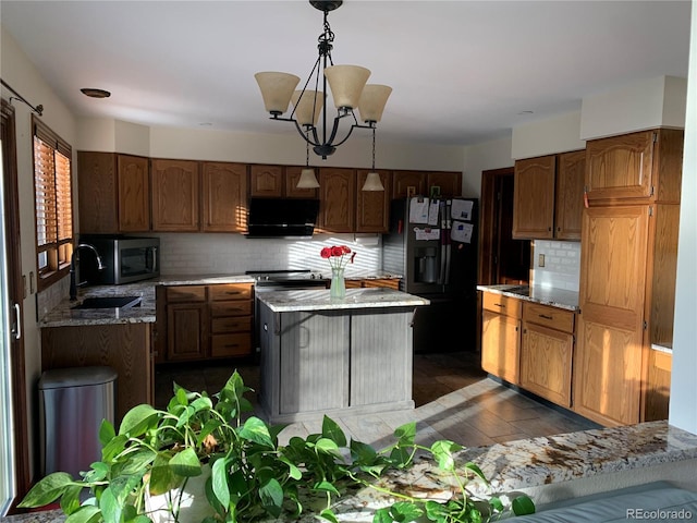 kitchen with a sink, stainless steel microwave, light stone counters, and black fridge