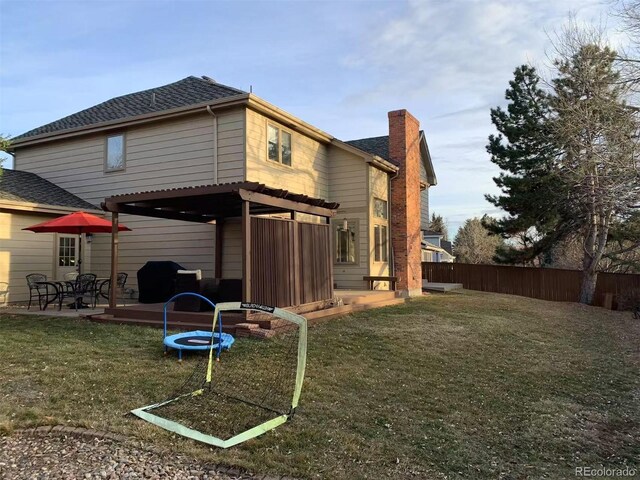 rear view of house with roof with shingles, fence, a chimney, and a lawn