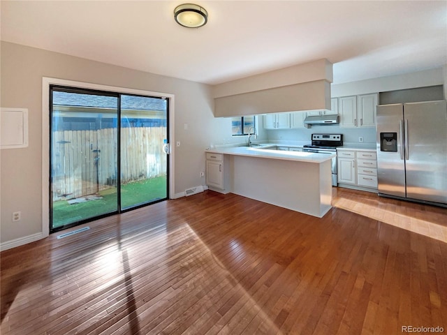 kitchen with sink, kitchen peninsula, appliances with stainless steel finishes, white cabinets, and hardwood / wood-style flooring