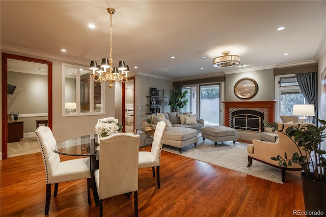 dining room with a tiled fireplace, crown molding, and hardwood / wood-style floors