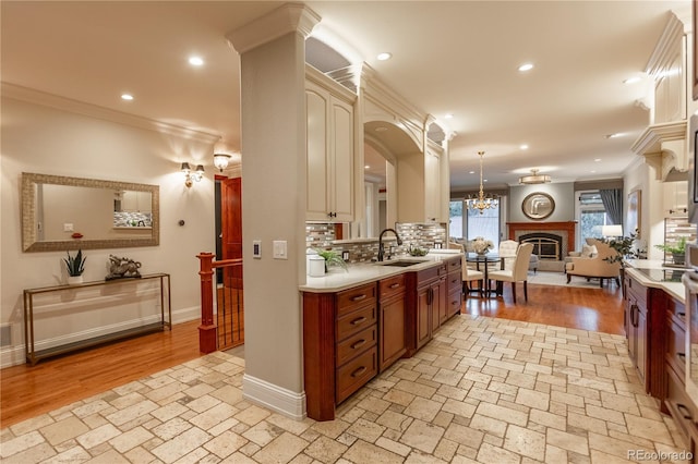 kitchen with tasteful backsplash, hanging light fixtures, crown molding, sink, and decorative columns