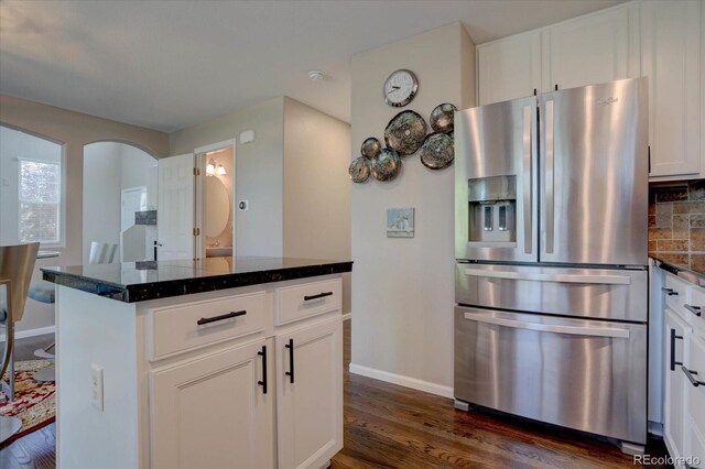 kitchen with dark stone counters, white cabinets, decorative backsplash, dark hardwood / wood-style floors, and stainless steel refrigerator with ice dispenser