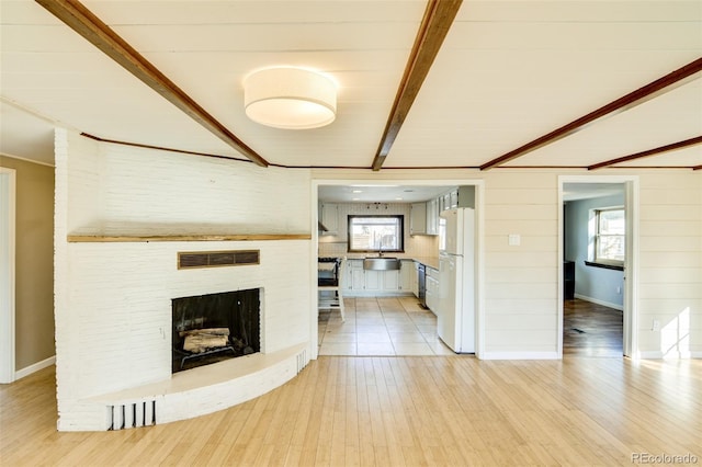 unfurnished living room with sink, beam ceiling, a fireplace, and light hardwood / wood-style floors