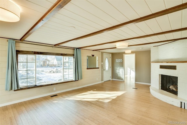 unfurnished living room featuring wood-type flooring, a brick fireplace, beam ceiling, and wood walls