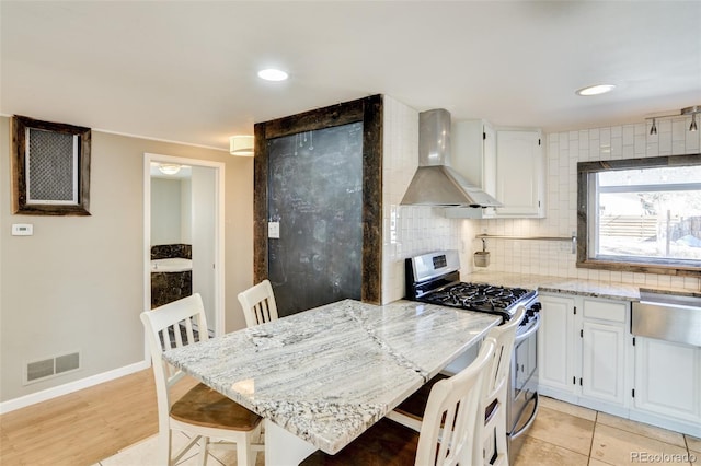 kitchen with white cabinetry, stainless steel range with gas stovetop, wall chimney exhaust hood, and a kitchen bar