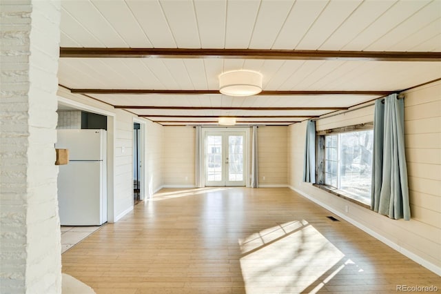 spare room featuring beam ceiling, french doors, light wood-style floors, and plenty of natural light
