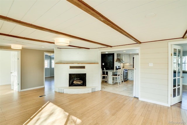 living room with visible vents, a brick fireplace, baseboards, wood finished floors, and beam ceiling