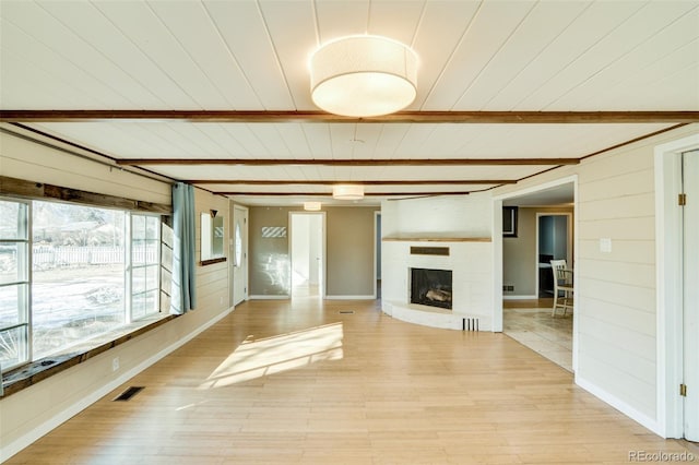 unfurnished living room with light wood-style flooring, beam ceiling, wooden walls, visible vents, and a brick fireplace