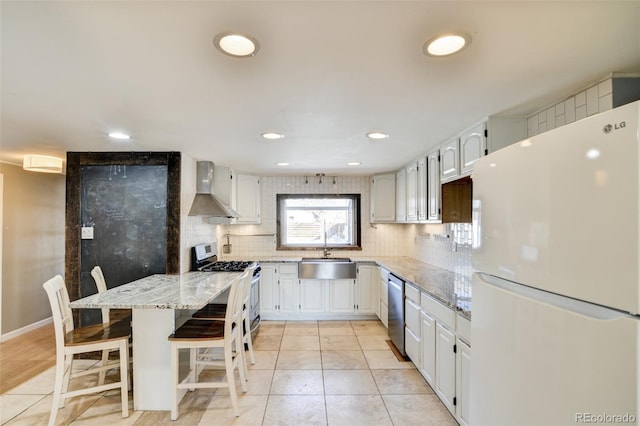 kitchen featuring tasteful backsplash, stainless steel appliances, a sink, light stone countertops, and wall chimney exhaust hood