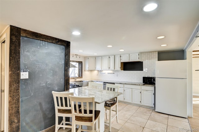 kitchen with a sink, backsplash, black microwave, freestanding refrigerator, and white cabinets
