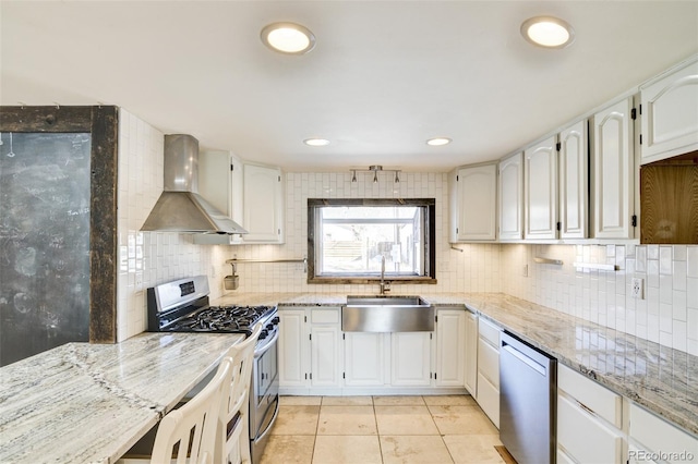 kitchen with a sink, light stone countertops, stainless steel appliances, and wall chimney exhaust hood