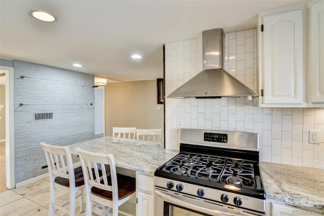 kitchen with white cabinetry, light tile patterned floors, gas stove, light stone counters, and wall chimney exhaust hood