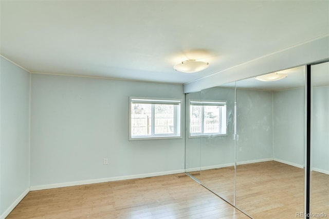 unfurnished bedroom featuring wood-type flooring, baseboards, and a closet