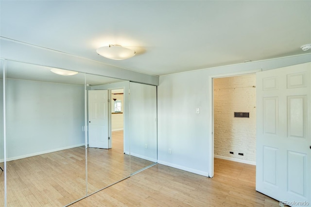 unfurnished bedroom with baseboards, light wood-style flooring, and brick wall
