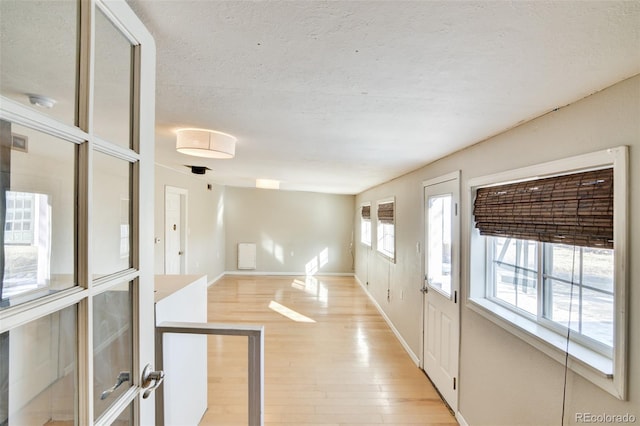 foyer with light wood finished floors, baseboards, and a textured ceiling