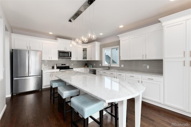 kitchen featuring hanging light fixtures, white cabinets, a kitchen island, sink, and stainless steel appliances