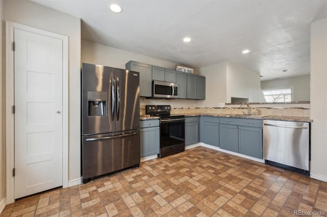 kitchen featuring baseboards, brick floor, stainless steel appliances, a sink, and recessed lighting