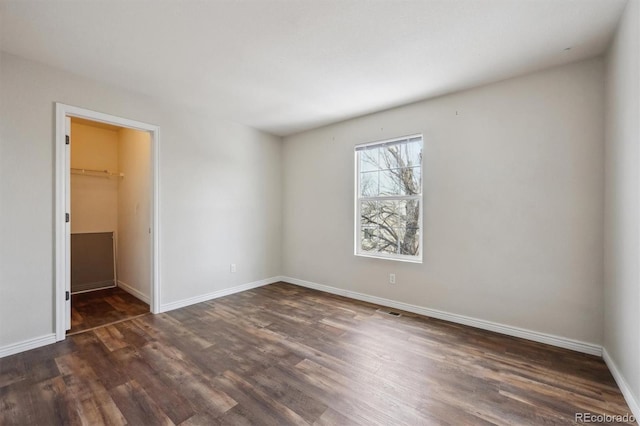 unfurnished bedroom with a closet, a spacious closet, baseboards, and dark wood-style flooring