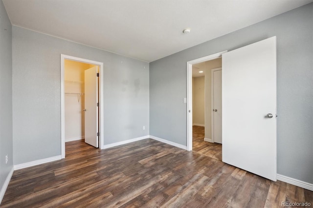 unfurnished bedroom featuring a closet, dark wood finished floors, a spacious closet, and baseboards