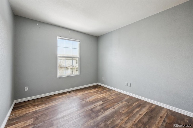 unfurnished room featuring dark wood-type flooring, visible vents, and baseboards