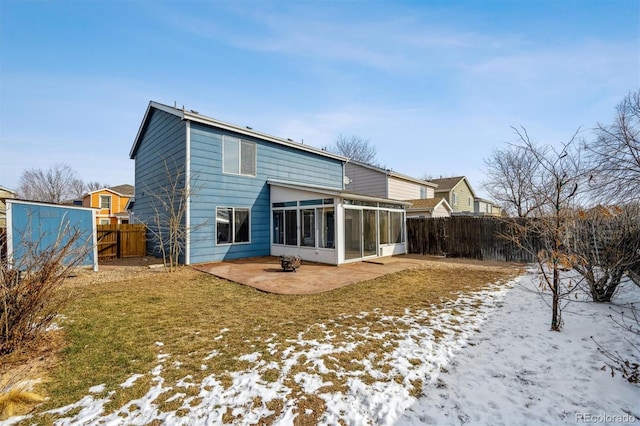 snow covered house featuring a yard, a patio area, a fenced backyard, and a sunroom