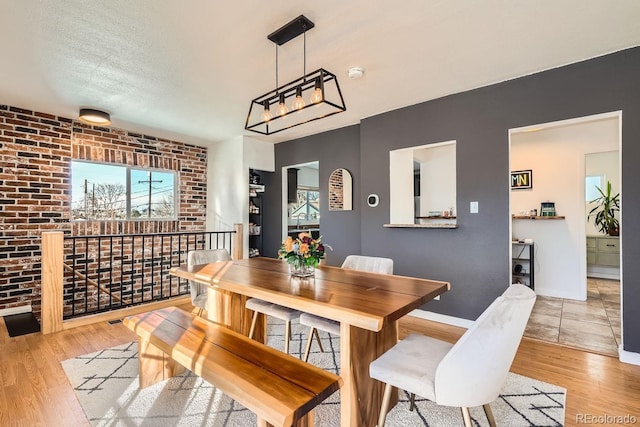 dining room featuring brick wall, a textured ceiling, and light wood-type flooring