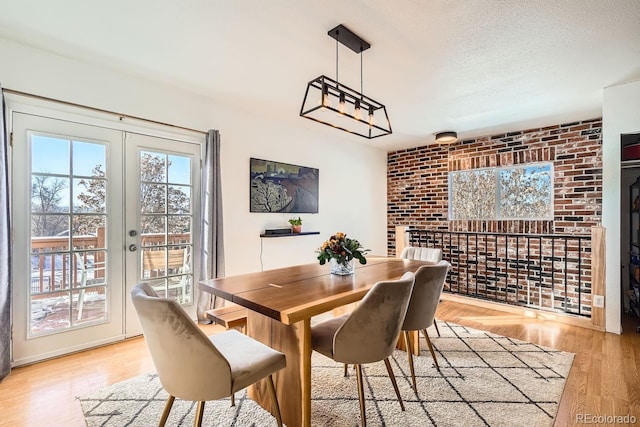 dining room with french doors, brick wall, light hardwood / wood-style floors, and a textured ceiling