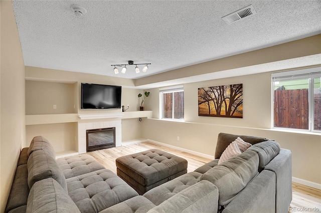 2140 W 135th Ave, Westminster, CO 80234 - living room featuring light wood-style flooring, a textured ceiling, baseboards, a tile fireplace, and rail lighting