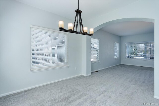 carpeted spare room featuring baseboards and arched walkways