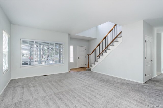 unfurnished living room featuring stairway, baseboards, and carpet
